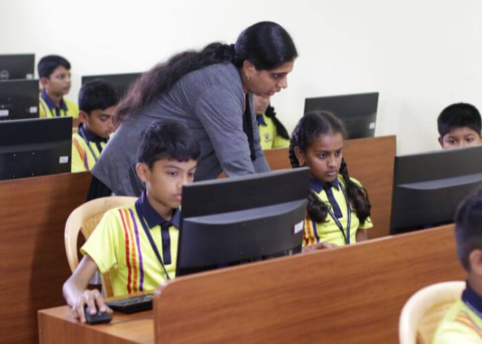 Dedicated teacher assisting students during a computer class at a leading school in North Bangalore.