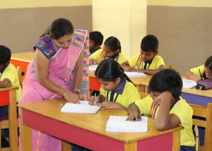 Primary students engaged in focused classroom learning with teacher guidance at NewAge World School, Bangalore.