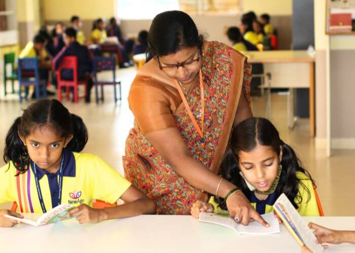 Teacher assisting students in the library at NewAge World School, International School in Yelahanka, nurturing academic growth.